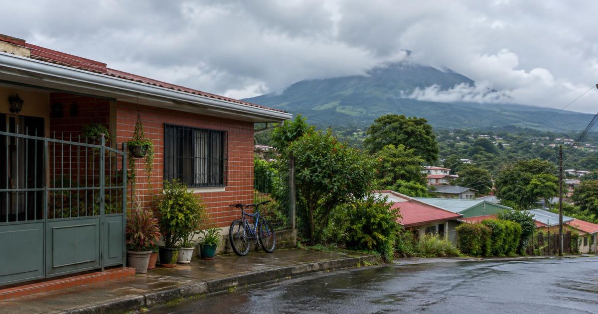 Brick house on a raised street in Alajuela, with rooftops, trees and the Poás volcano slopes behind