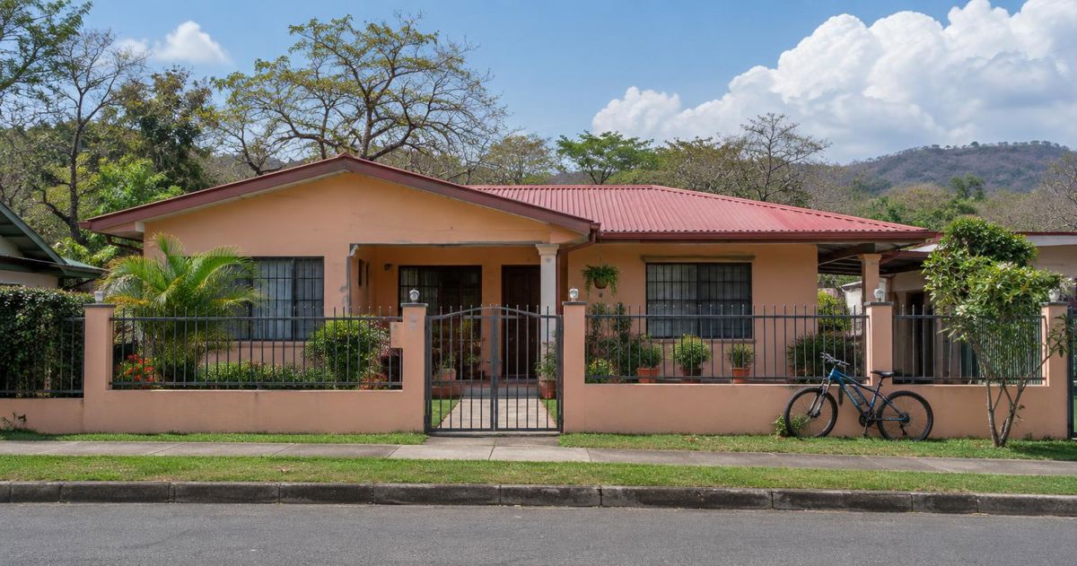 Casa color durazno con portón y jardín pequeño en una calle de Liberia, Guanacaste, bajo nubes de la mañana